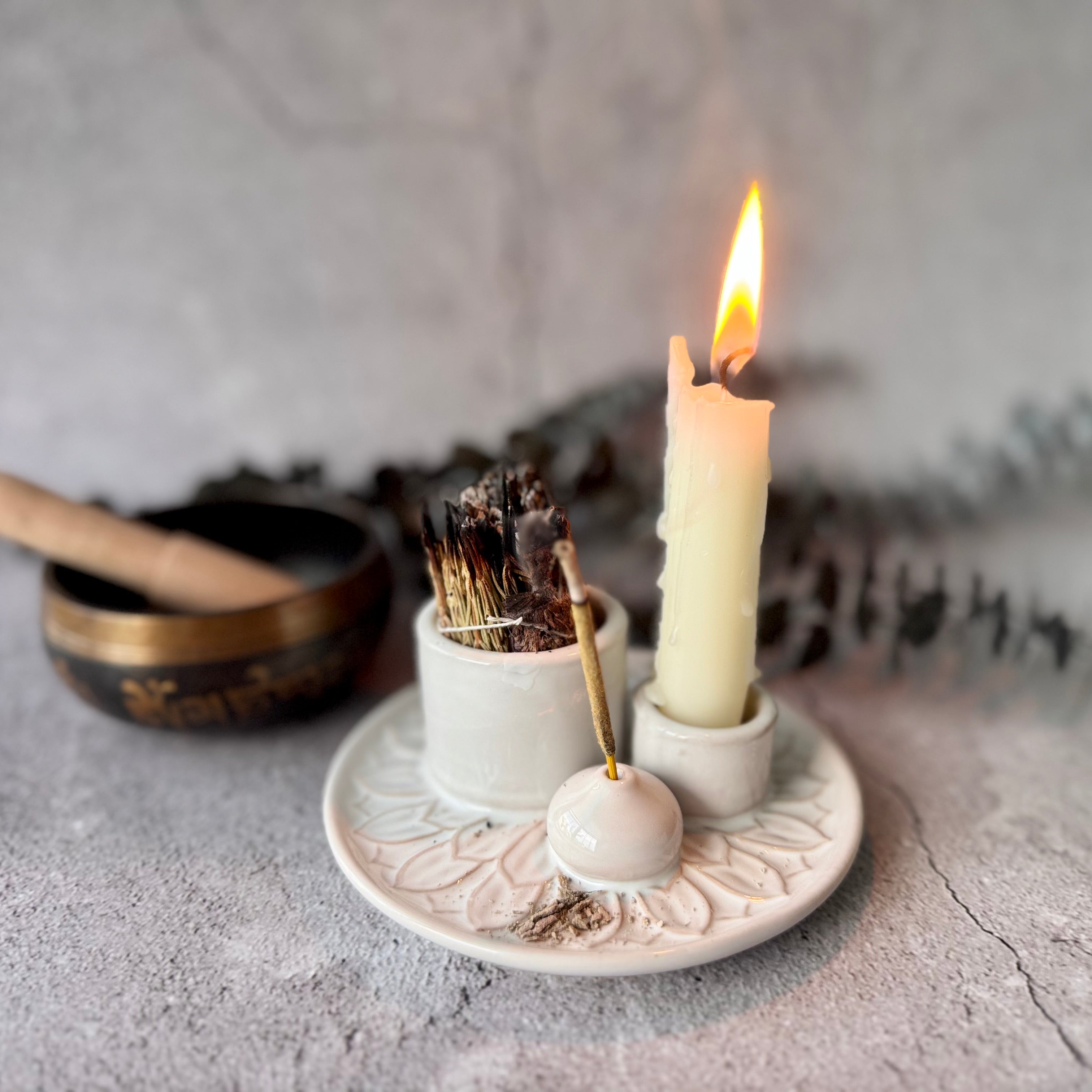 Candle on a white ceramic holder with a small bowl of incense and a singing bowl in the background.