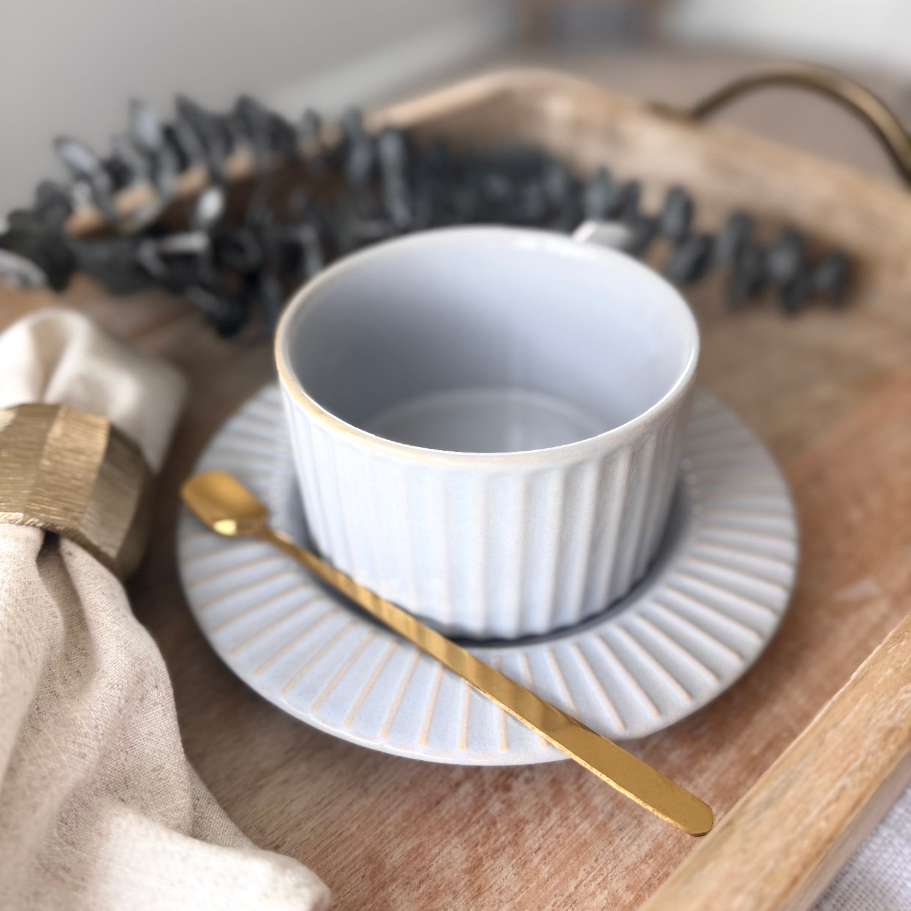 Calming light gray glaze with soft blue undertones ceramic cup and saucer with gold spoon on a wooden tray